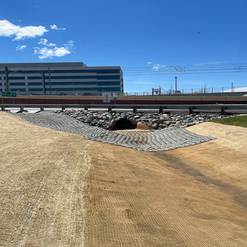 Rock-lined drainage culvert beside road, offices, and power lines.