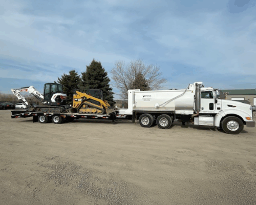White dump truck hauling trailer with excavator and loader.
