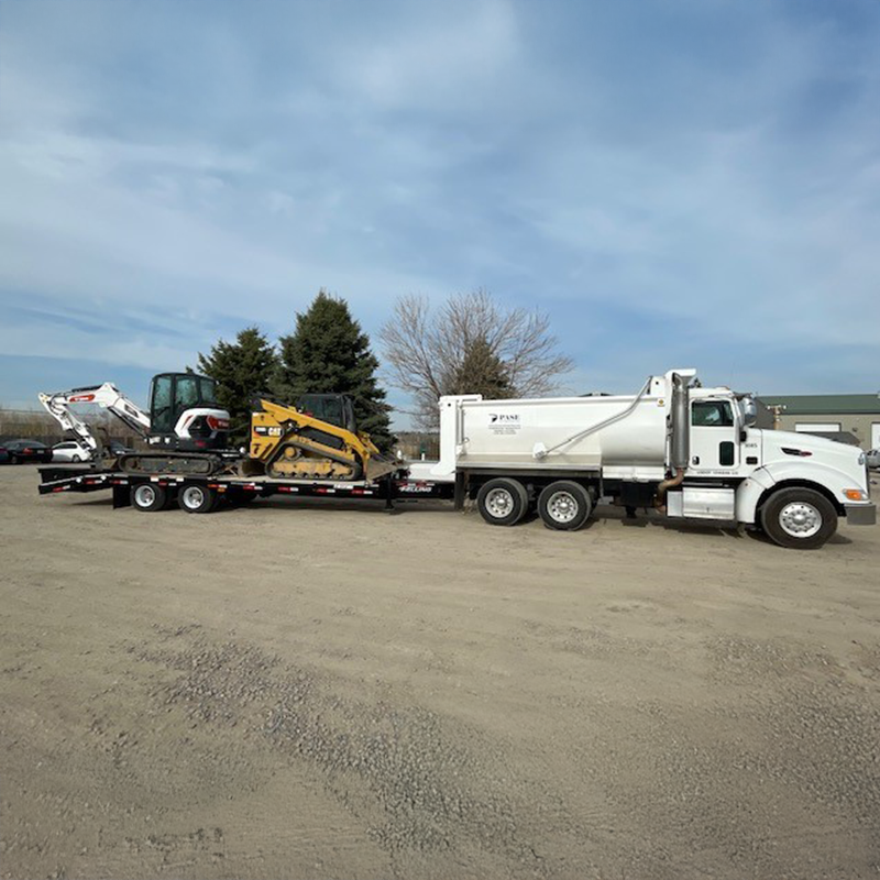 White dump truck hauling trailer with excavator and loader.