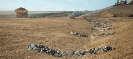 Construction site with rock mounds and machinery in the background.