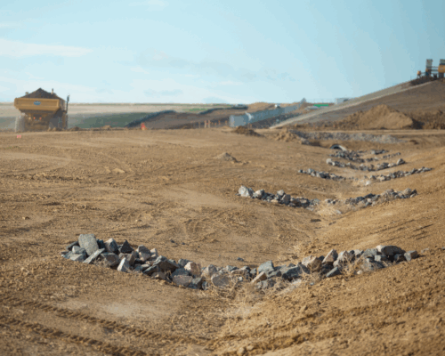 Construction site with rock mounds and machinery in the background.