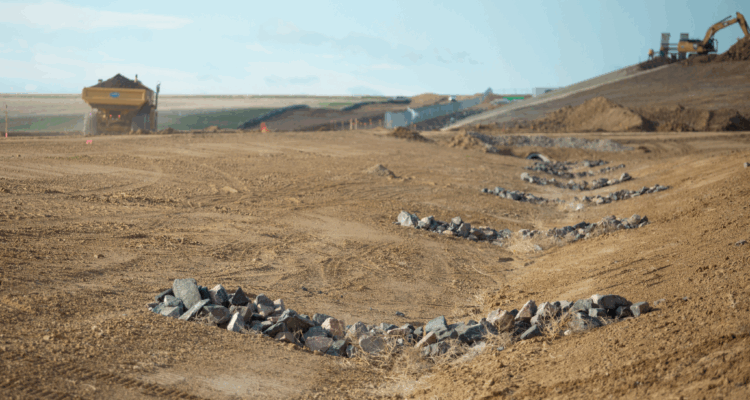 Construction site with rock mounds and machinery in the background.