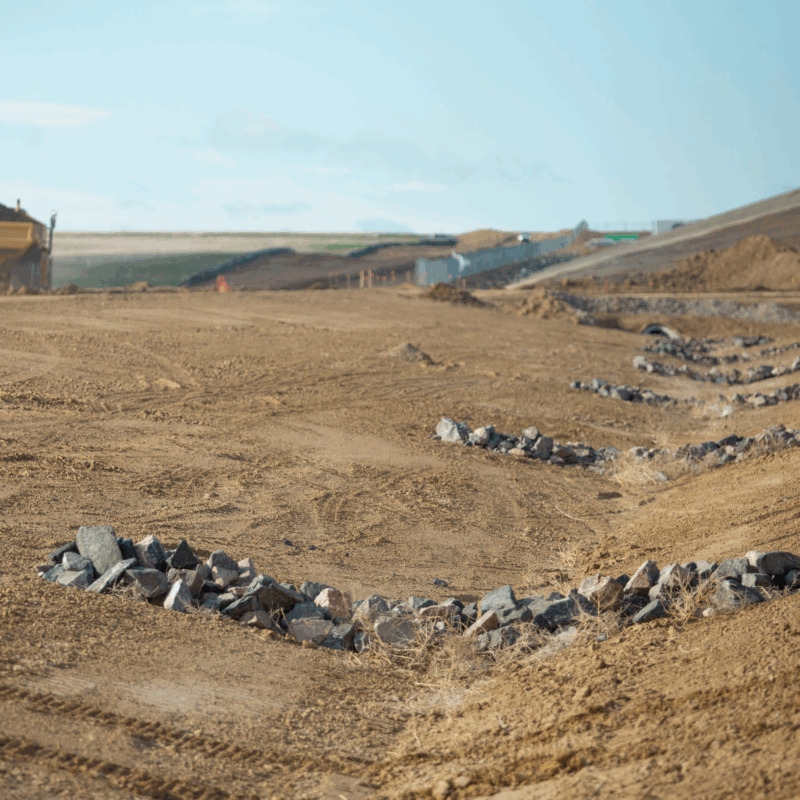 Construction site with rock mounds and machinery in the background.