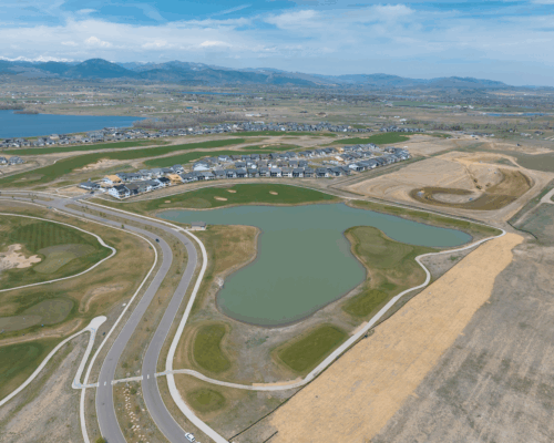 Aerial view of suburb with houses, pond, and mountain backdrop.
