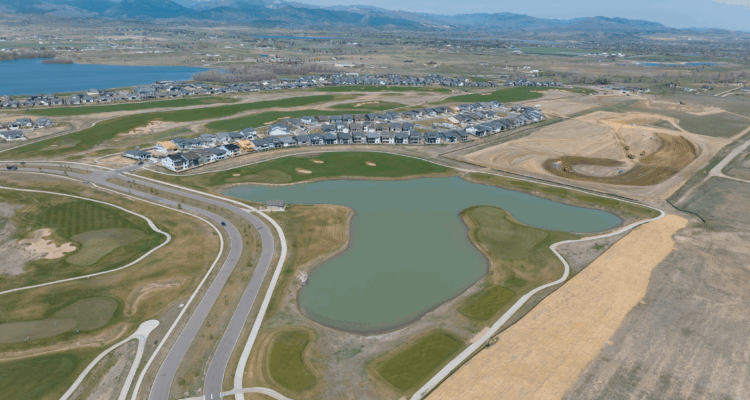 Aerial view of suburb with houses, pond, and mountain backdrop.