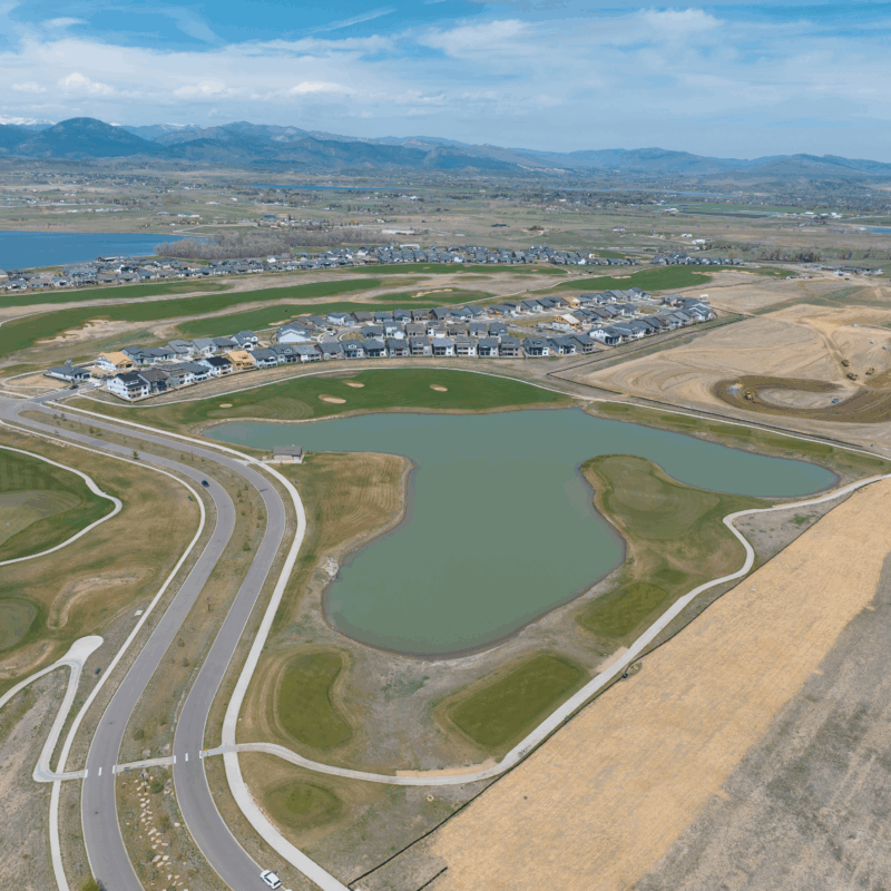 Aerial view of suburb with houses, pond, and mountain backdrop.