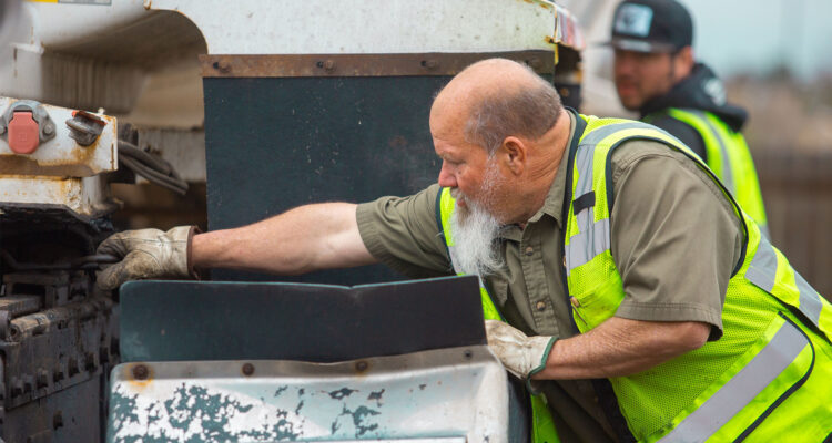 Worker in yellow vest inspects outdoor machinery; another stands behind.