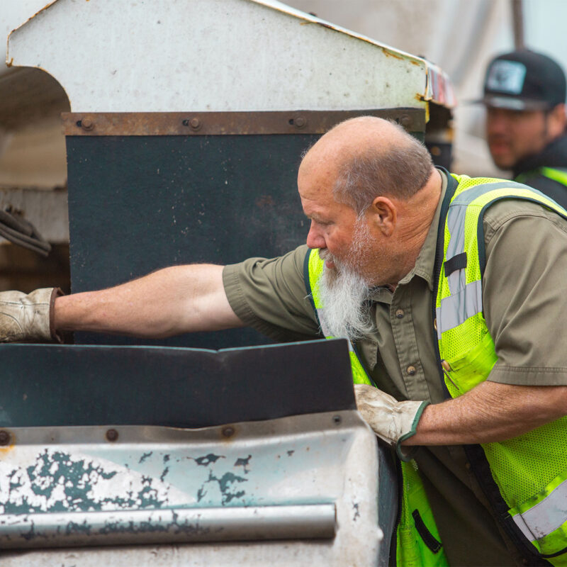 Worker in yellow vest inspects outdoor machinery; another stands behind.