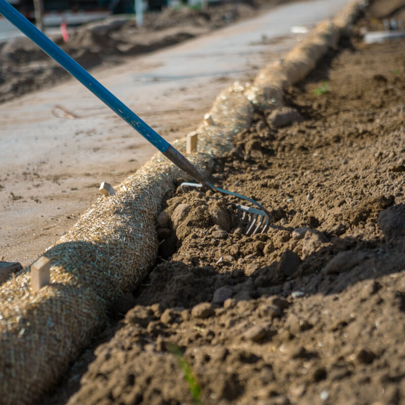 Person raking soil next to a sidewalk.