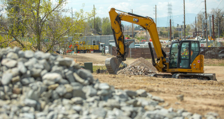 Yellow excavator moving dirt, rocks, with workers in background.