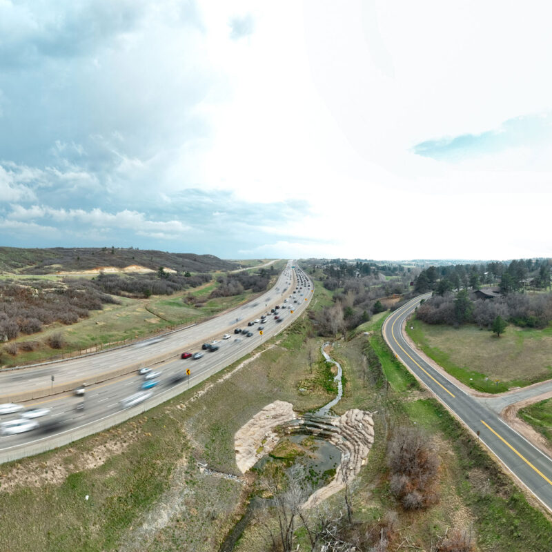 Busy highway on left with blurred cars, empty road and houses on right.
