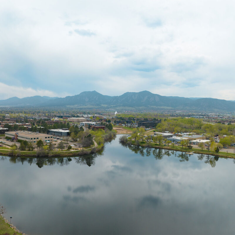 Aerial view of lake surrounding by buildings and trees with mountain backdrop.
