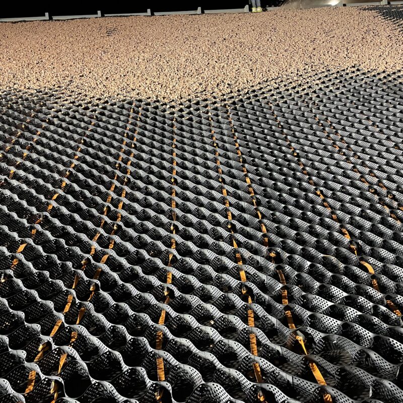 Black geocell grid with gravel, forming a wavy surface.