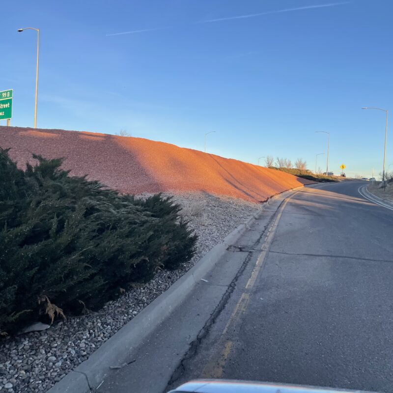 Curving paved road, street sign, pink gravel, clear sky.