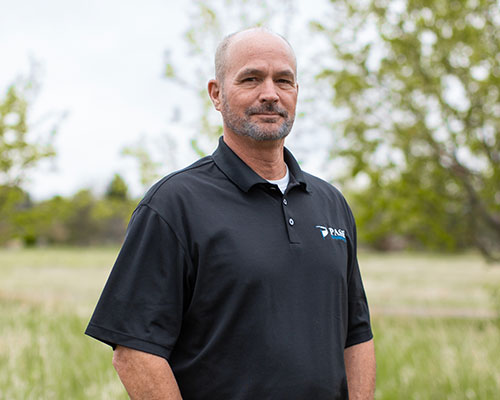 Man in black logo polo smiles in grassy field.