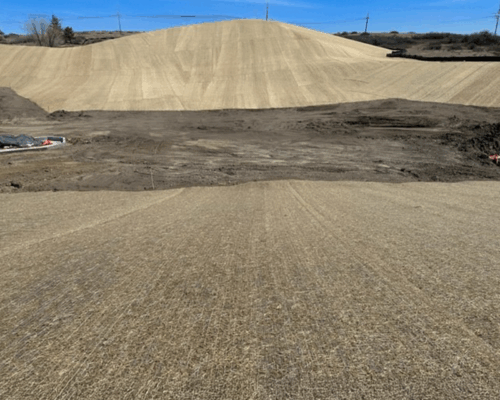 Graded dirt hill with straw matting under blue sky.