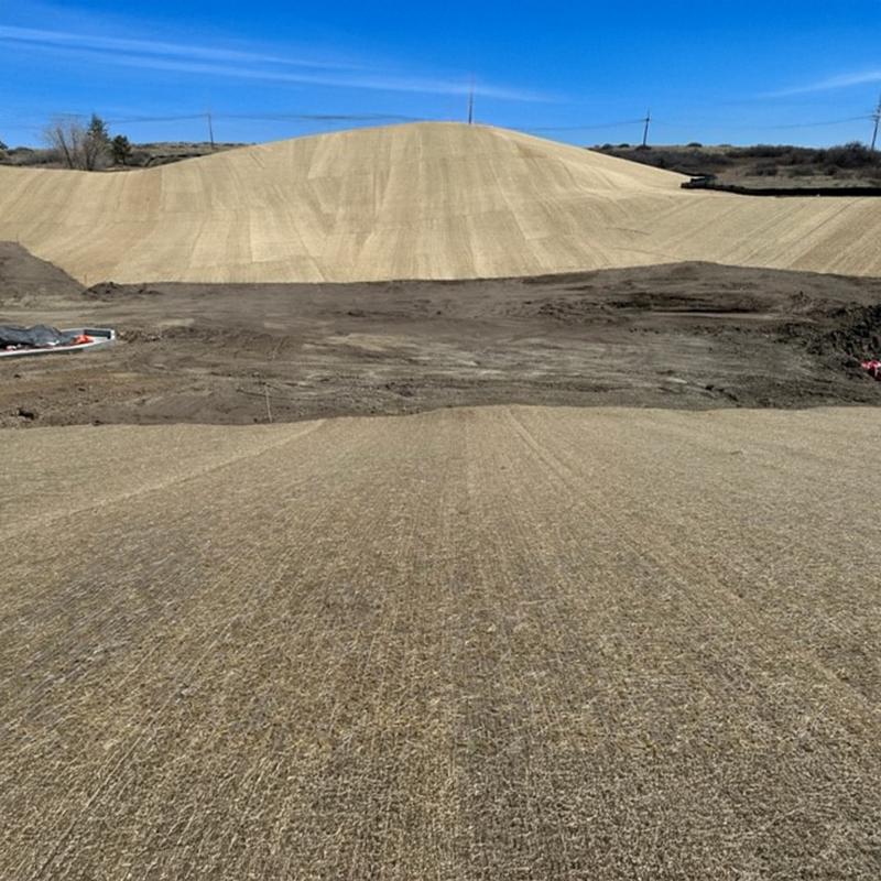 Graded dirt hill with straw matting under blue sky.