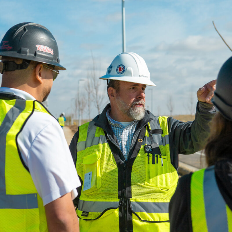 Supervisor in safety vest and hard hat gestures to workers.