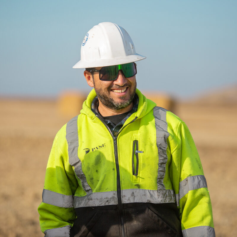 Man in white hard hat and yellow jacket at worksite.